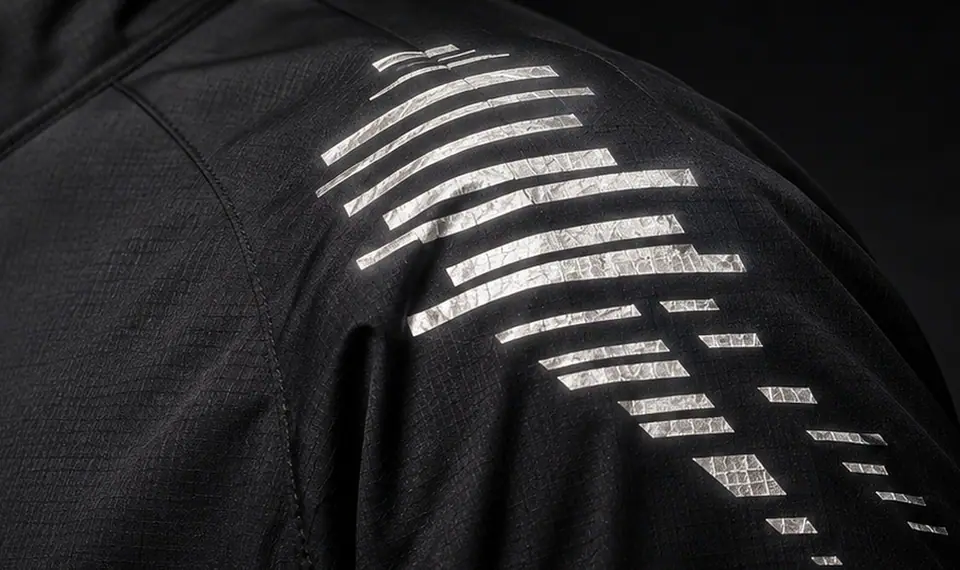 Retroreflective broken-stripe print flaring white-silver across the shoulder of a black running jacket